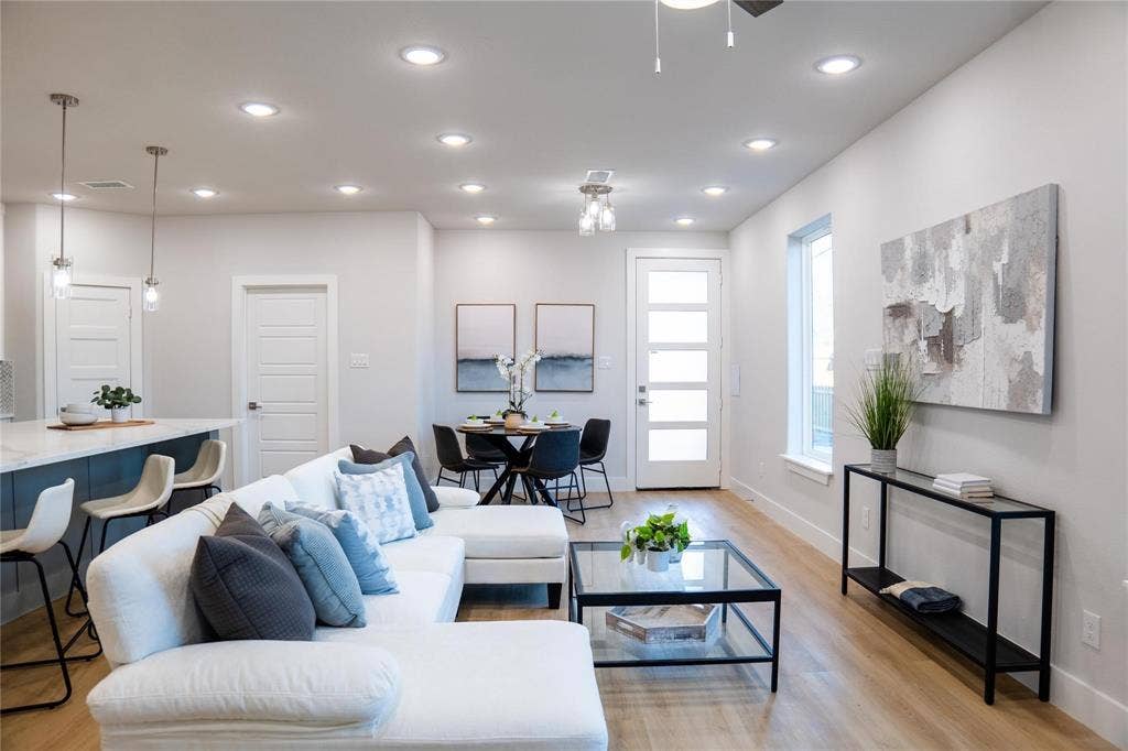 Open-concept interior featuring wood-finish flooring, recessed lighting, a central island with waterfall-edge countertop, and a multi-pane glass entry door