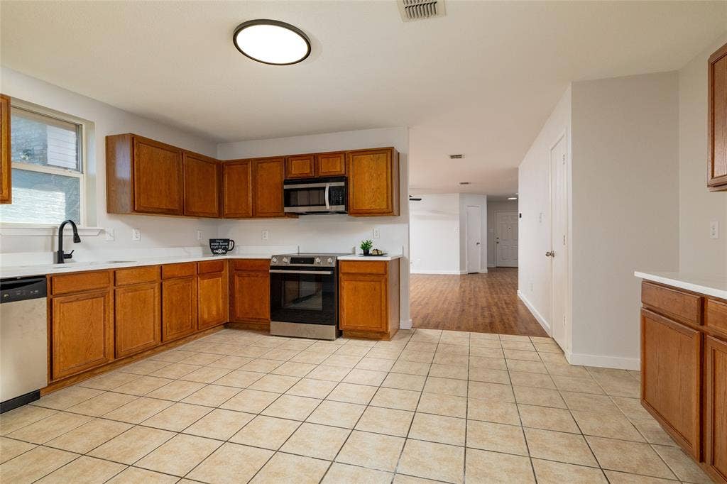 Kitchen featuring wood cabinetry, stainless steel appliances, white countertops, tile flooring, and a matte black faucet