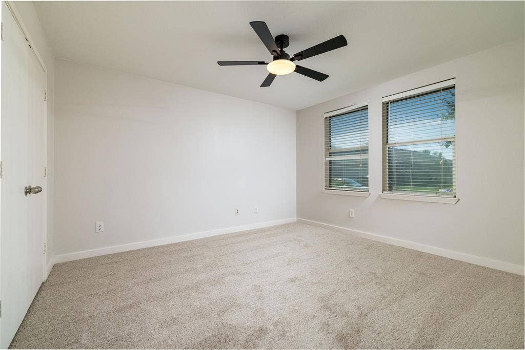 Interior space featuring neutral wall-to-wall carpeting, dual-pane windows with horizontal blinds, and a matte black ceiling fan with an integrated light fixture