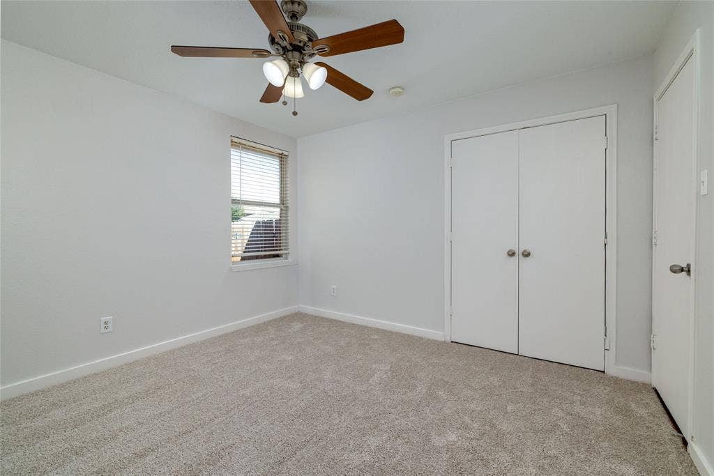 Neutral-toned wall-to-wall carpeting, ceiling fan with integrated lighting, single-pane window with horizontal blinds, and double-door closet