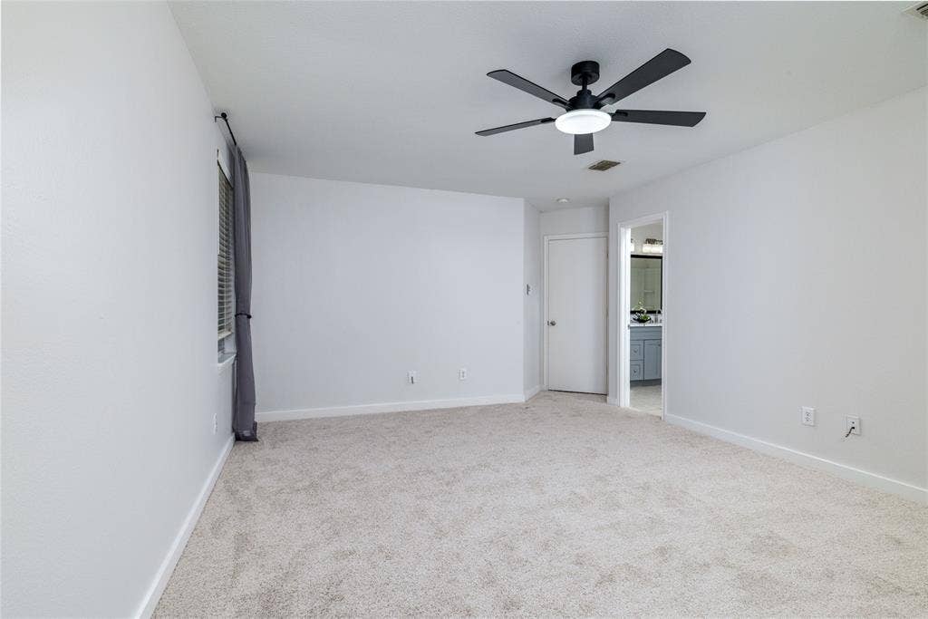 Interior room featuring neutral wall-to-wall carpeting, a matte black multi-blade ceiling fan with integrated LED lighting, and a doorway opening to a secondary space