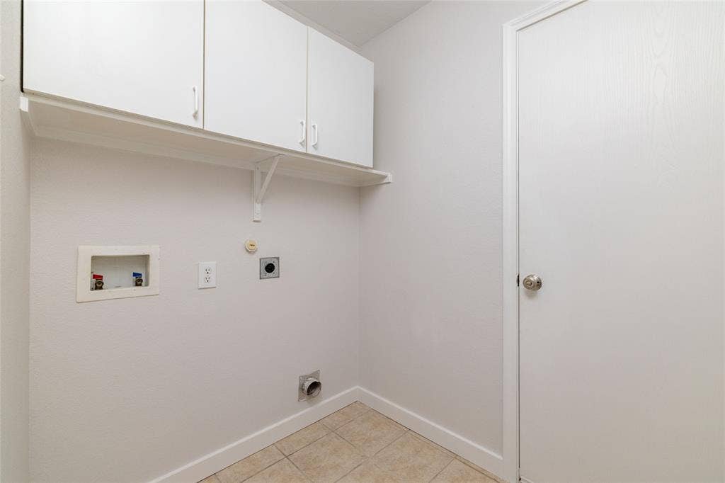 Utility space featuring wall-mounted white cabinetry, open shelving, tile flooring, and a solid-core interior door