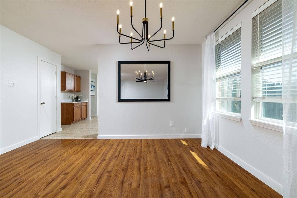 Wood-finish flooring, multi-arm metal chandelier, and large dual windows with horizontal blinds