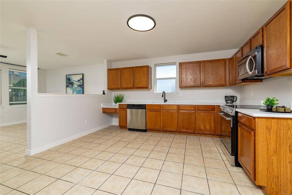 Kitchen featuring wood cabinetry, white countertops, stainless steel appliances, ceramic tile flooring, and a matte black faucet