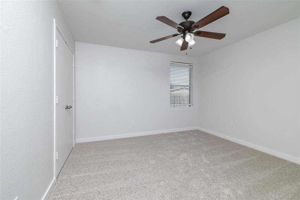 Neutral interior featuring wall-to-wall carpeting, a multi-blade ceiling fan with integrated lighting, and a single-pane window with horizontal blinds