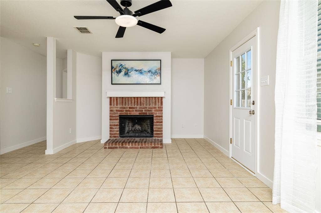 Red brick fireplace with a mantle, tile flooring, ceiling fan, and exterior door with glass panes