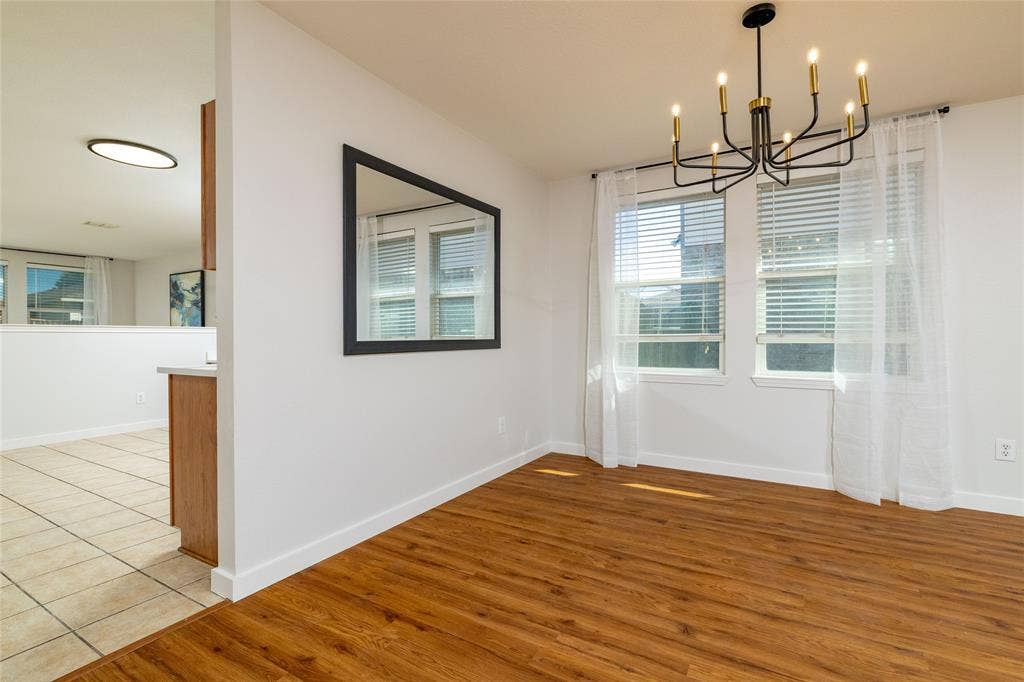 Wood-finish flooring, matte black multi-arm chandelier, dual windows with horizontal blinds, and a large wall-mounted mirror