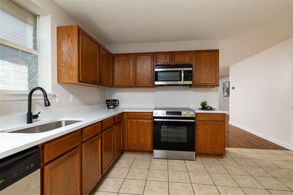 Kitchen featuring wood cabinetry, white countertops, stainless steel appliances, a matte black faucet, and tile flooring