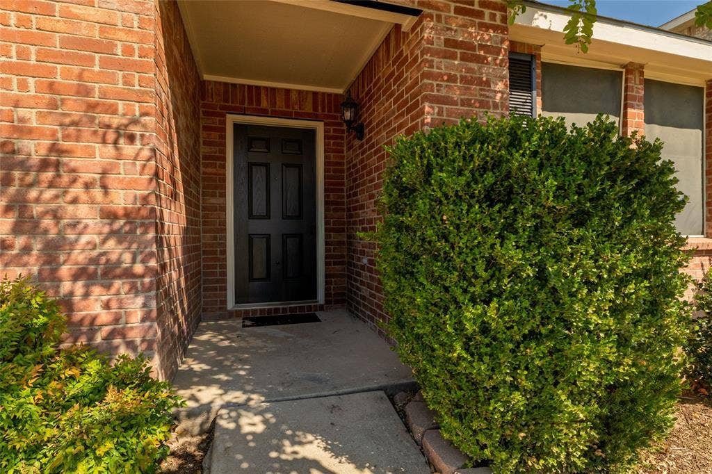 Brick exterior entry featuring a six-panel front door, covered porch, and integrated exterior light fixture