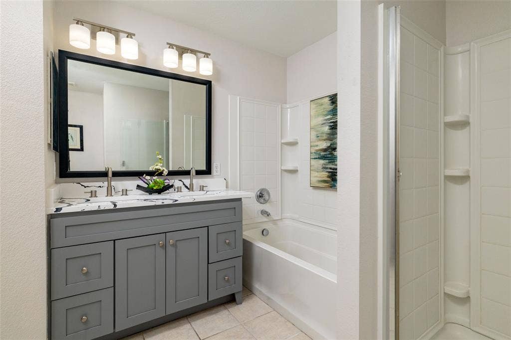 Dual-sink vanity with veined stone-finish countertop, Shaker-style cabinetry, framed vanity mirror, integrated bathtub-shower combination, and separate glass-enclosed shower stall
