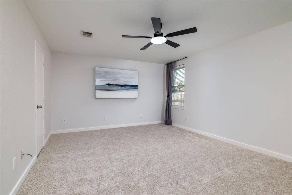 Neutral-toned interior space featuring light-colored wall-to-wall carpeting, a matte black multi-blade ceiling fan with integrated lighting, and a single-pane window