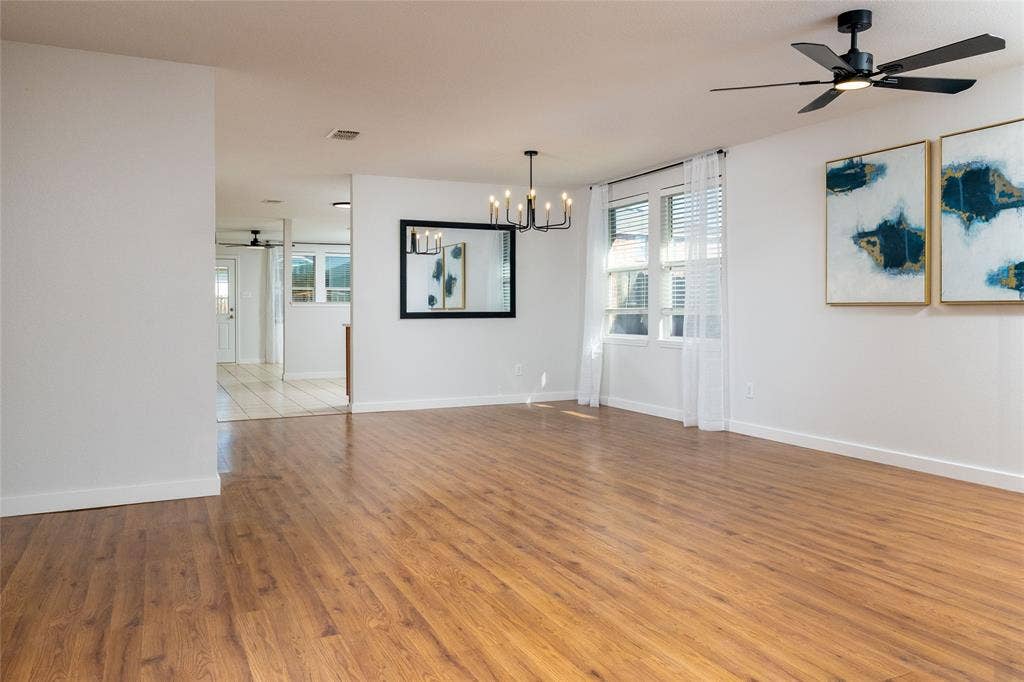 Open living area featuring wood-finish flooring, a multi-arm chandelier, and a matte black ceiling fan with integrated lighting