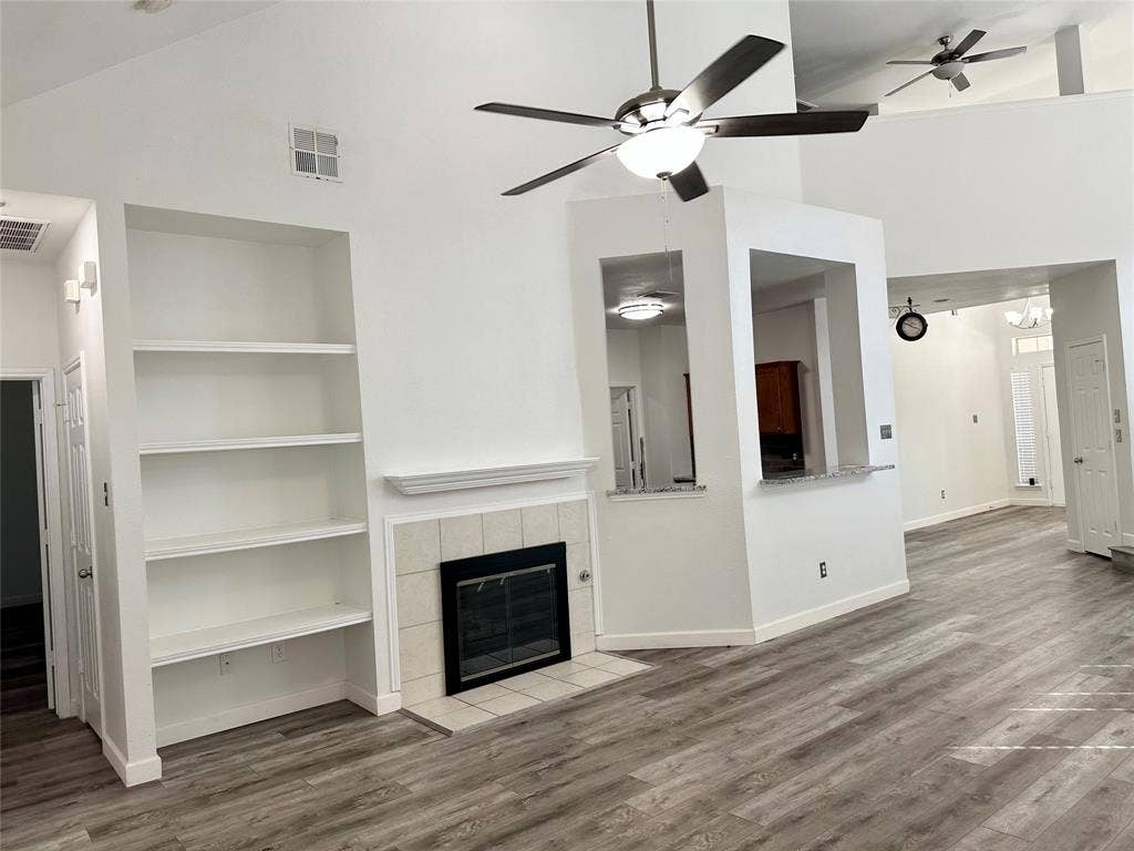 9756 Old Field Drive, McKinney, TX 75072 Vaulted ceilings with recessed lighting, tile-surround fireplace, built-in shelving, hard-surface flooring, and kitchen pass-through counter