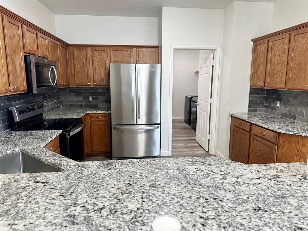 9756 Old Field Drive, McKinney, TX 75072 Kitchen featuring wood cabinetry, stone countertops, dark rectangular tile backsplash, stainless steel appliances, and integrated microwave