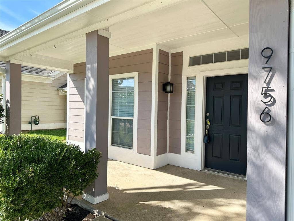 9756 Old Field Drive, McKinney, TX 75072 Covered entryway featuring horizontal lap siding, square support columns, a dark-toned solid core door with side light and transom window, and exterior wall-mounted lighting