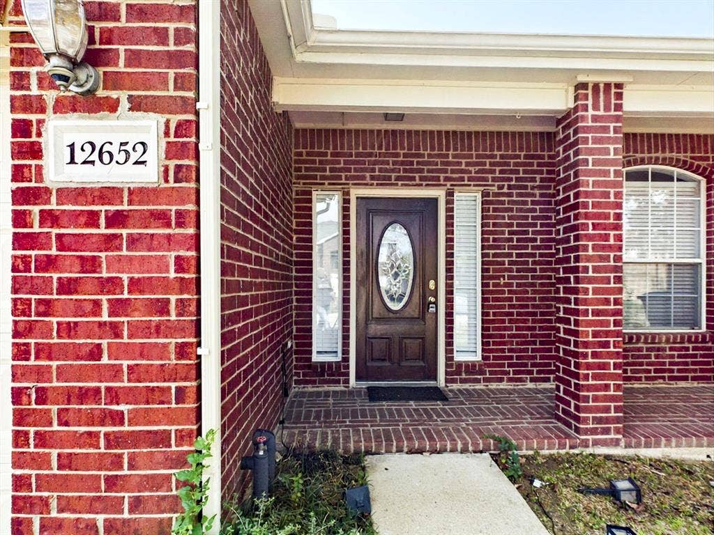 12652 Oakwood Circle, Fort Worth, TX 76040 Red brick exterior featuring a covered porch with matching brick flooring, arched window, and a wood-finish door with an oval glass insert and sidelights