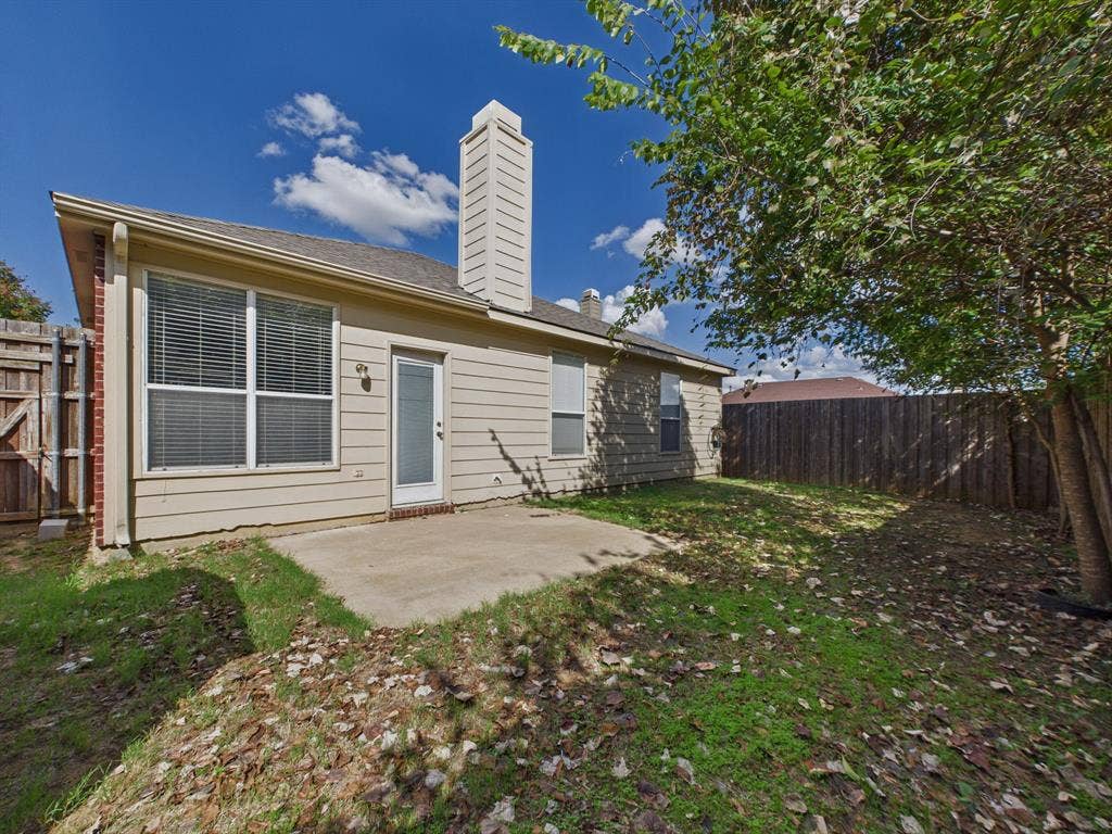 12652 Oakwood Circle, Fort Worth, TX 76040 Rear exterior featuring light-toned horizontal siding, a central chimney, a concrete patio, and a full-height wood privacy fence