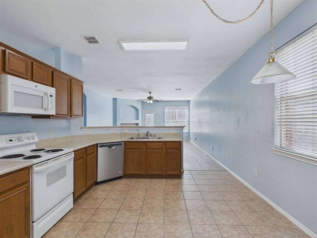 12652 Oakwood Circle, Fort Worth, TX 76040 Kitchen featuring stained wood cabinetry, solid surface countertops, stainless steel dishwasher, white range with overhead microwave, and ceramic tile flooring
