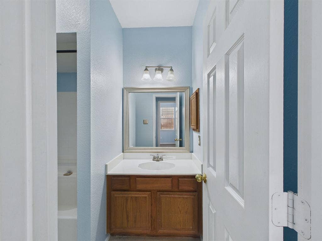 12652 Oakwood Circle, Fort Worth, TX 76040 Bathroom featuring a wood-finish vanity with a solid-surface countertop, an integrated sink, a framed wall mirror, and a three-light vanity fixture