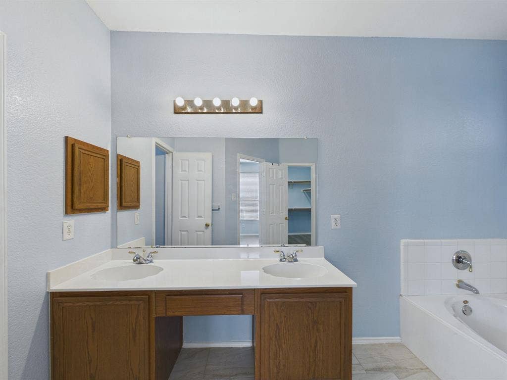 12652 Oakwood Circle, Fort Worth, TX 76040 Dual-sink vanity with white countertop, recessed basins, wood-finish cabinetry, full-width mirror, and five-bulb light fixture
