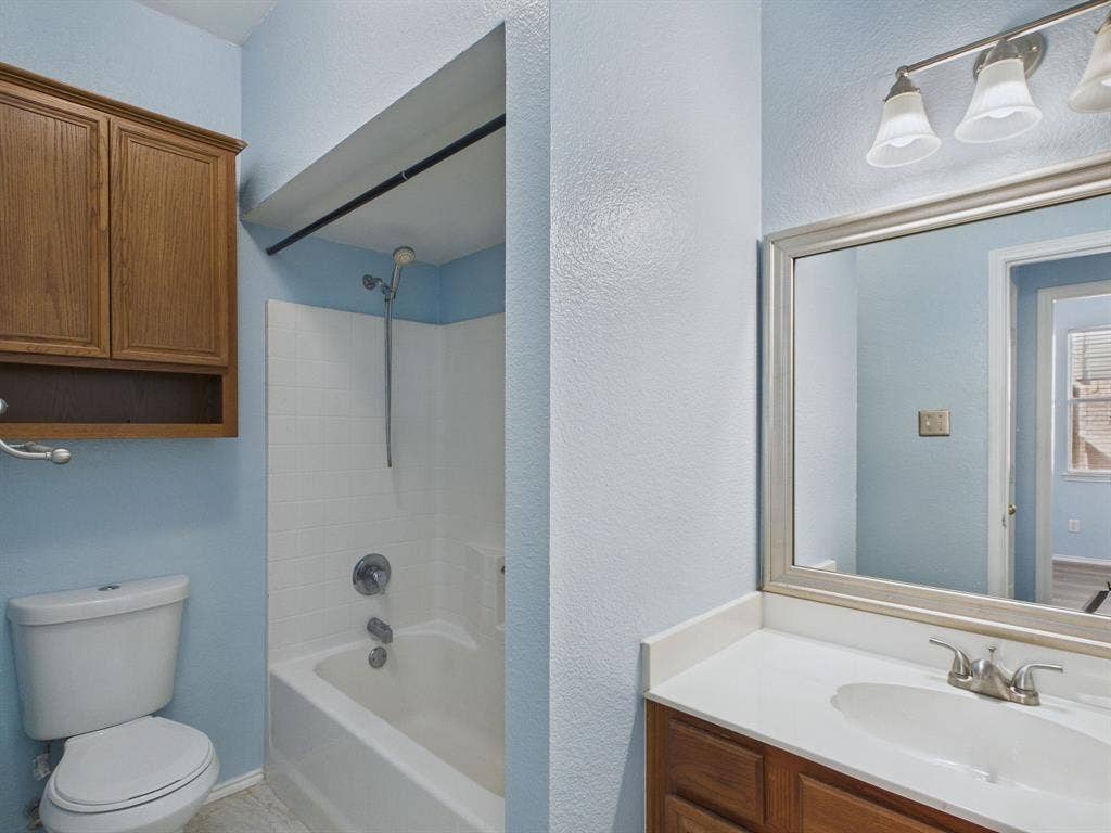 12652 Oakwood Circle, Fort Worth, TX 76040 Bathroom featuring wood-finish cabinetry, a white vanity countertop with integrated sink, a framed vanity mirror, three-light fixture, and a tub-shower combination with white surround