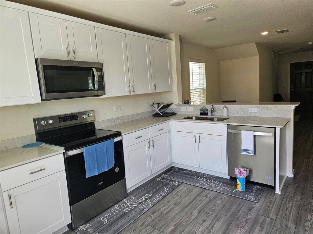 1860 Ballinger Drive, Forney, TX 75126 Kitchen featuring white Shaker-style cabinetry, stainless steel appliances, neutral stone-finish countertops, and wood-finish flooring