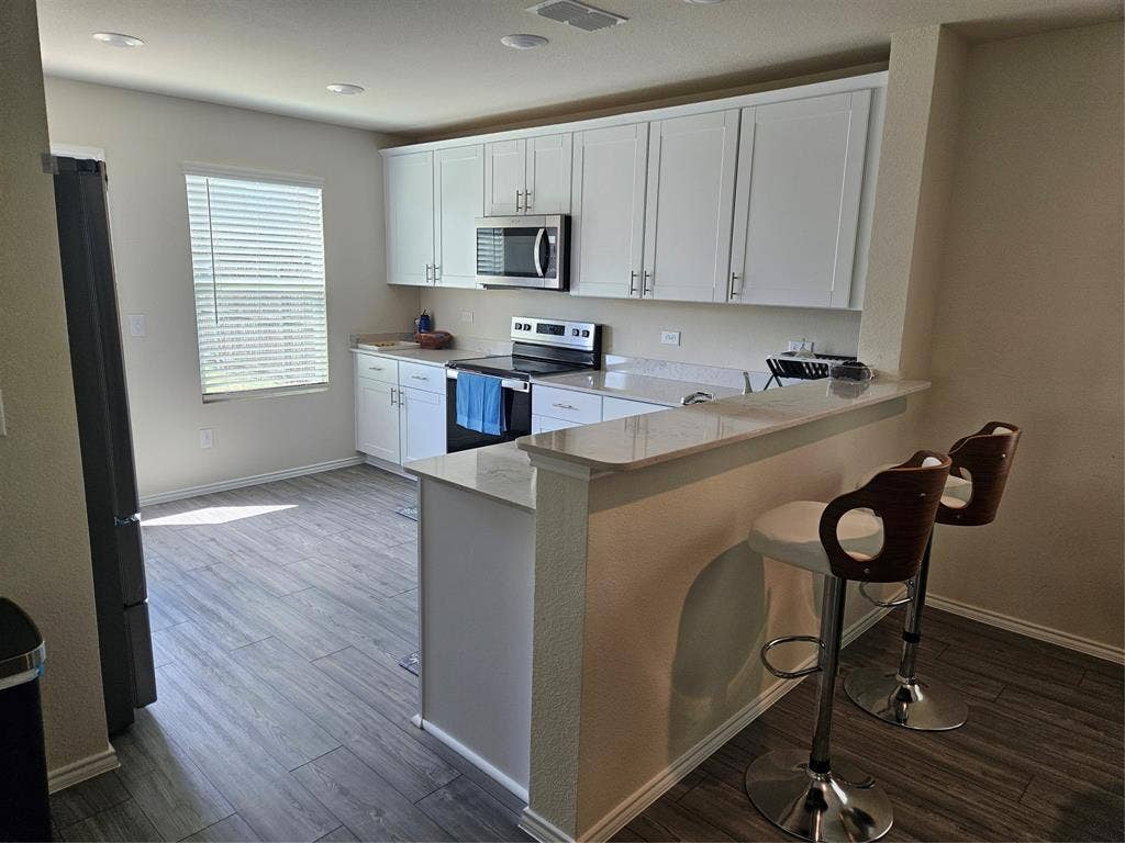1860 Ballinger Drive, Forney, TX 75126 Kitchen featuring white cabinetry, solid-surface countertops, wood-finish flooring, stainless steel appliances, and a peninsula breakfast bar