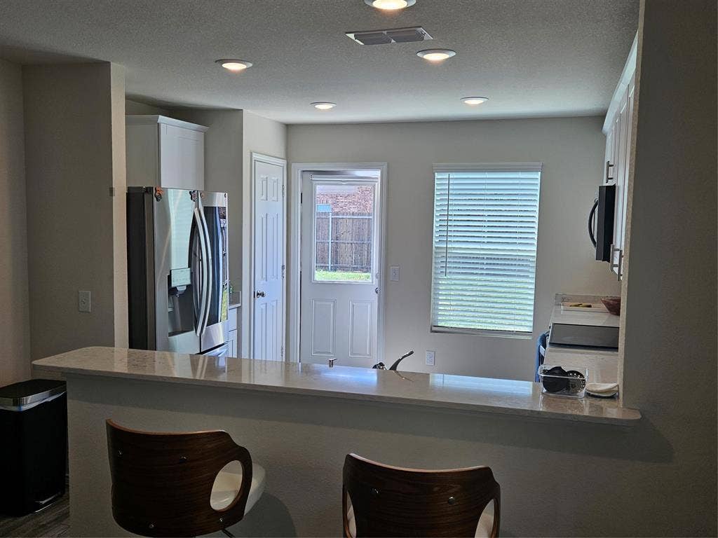 1860 Ballinger Drive, Forney, TX 75126 Kitchen featuring a breakfast bar with stone-surfaced countertop, stainless steel refrigerator, recessed lighting, and white cabinetry