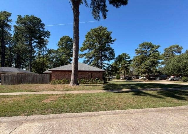 Brick exterior featuring a hip roof, wooden privacy fencing, and mature trees situated on a spacious corner lot
