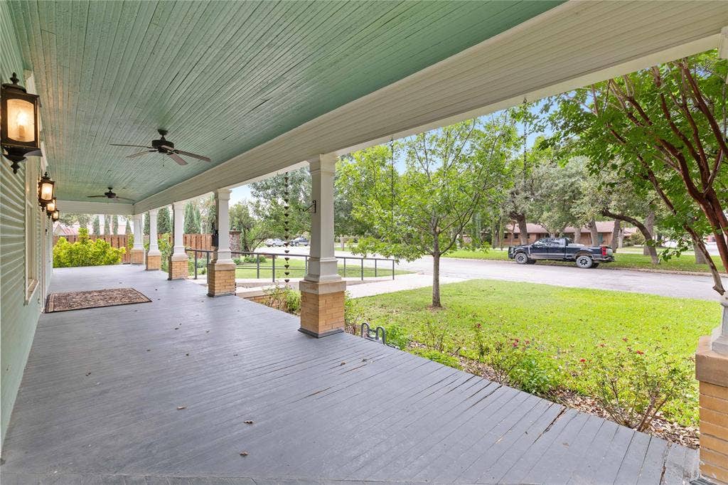 Covered wrap-around porch featuring wood-plank flooring, beadboard ceiling, brick-based columns, and wall-mounted exterior lighting