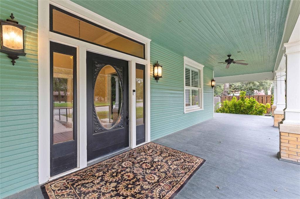 Covered front porch featuring horizontal lap siding, beadboard ceiling, recessed entry with elliptical glass door insert, transom window, and mounted wall lanterns