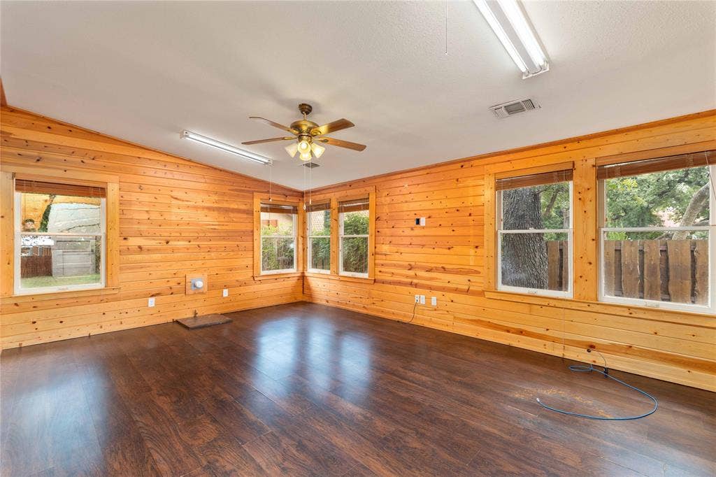 Interior featuring natural wood-paneled walls, dark wood-finish flooring, multiple windows, a ceiling fan with integrated light, and recessed strip lighting