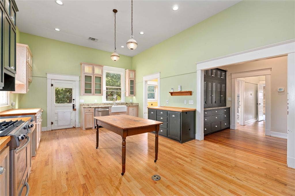 Kitchen featuring high ceilings, wood-finish flooring, stone-surfaced countertops, a farmhouse-style sink, and built-in cabinetry