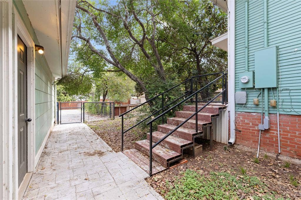 Exterior side yard featuring a concrete paver walkway, brick foundation, metal staircase with handrails, and a gated perimeter