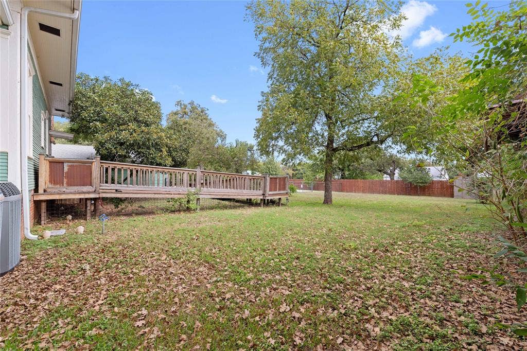 Expansive backyard featuring a wood deck, perimeter wood fencing, and mature trees