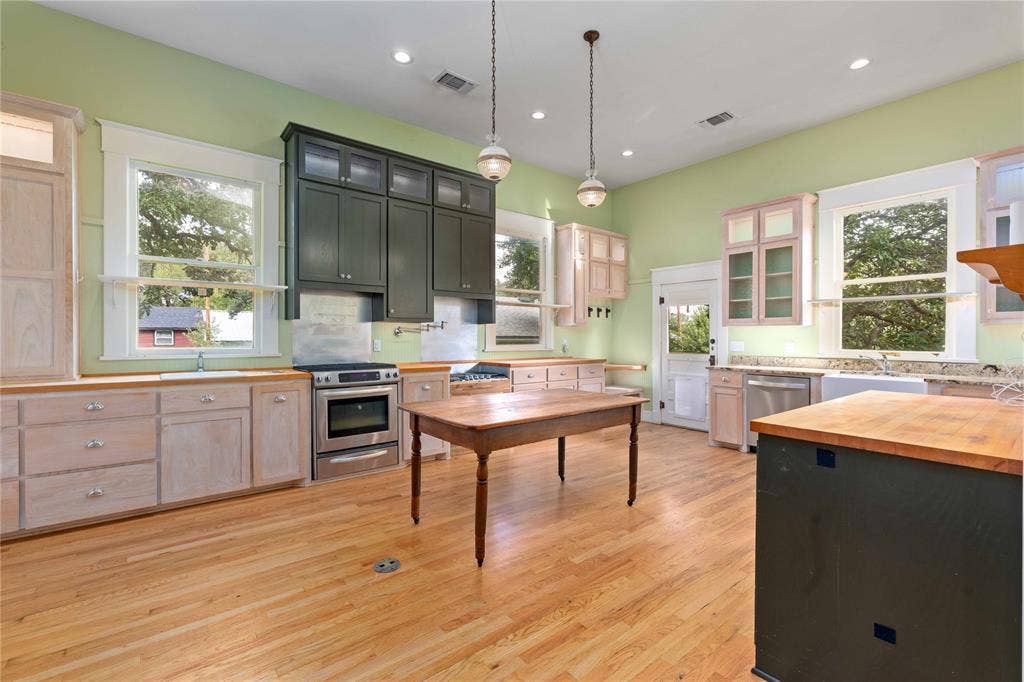 Kitchen featuring light wood-finish flooring, two-toned cabinetry with glass-front uppers, stainless steel oven, stone countertops, and recessed lighting