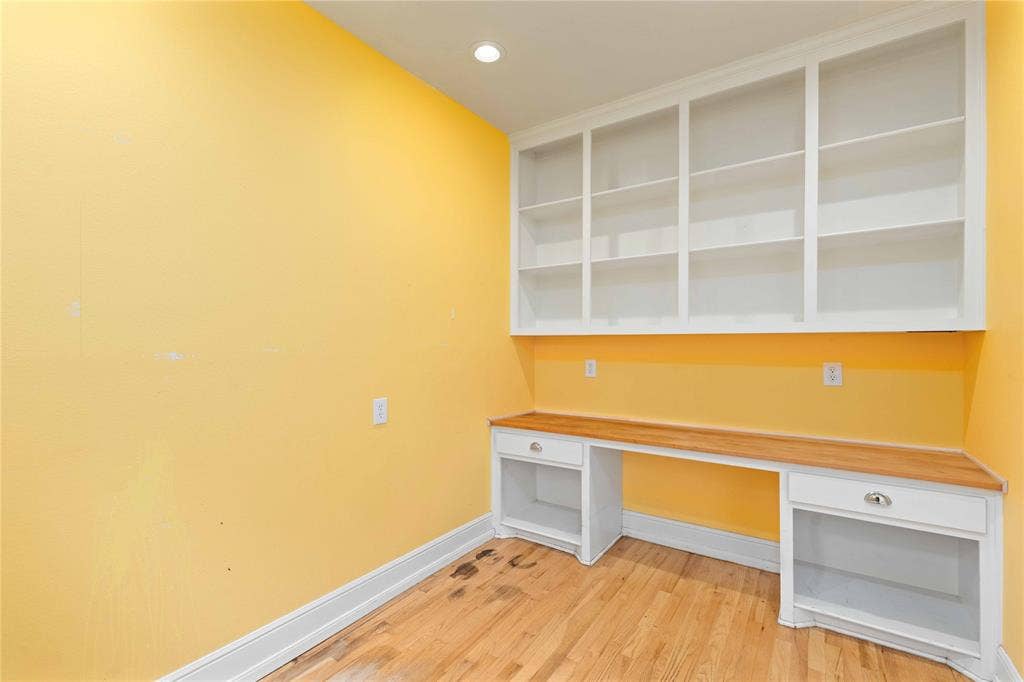 Built-in shelving, wood-surface desk with integrated drawers, and wood-finish flooring