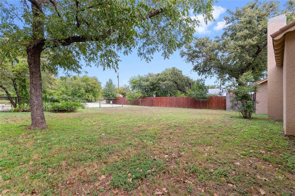 Spacious backyard featuring a grass lawn, mature trees, a wood privacy fence, and a chimney structure
