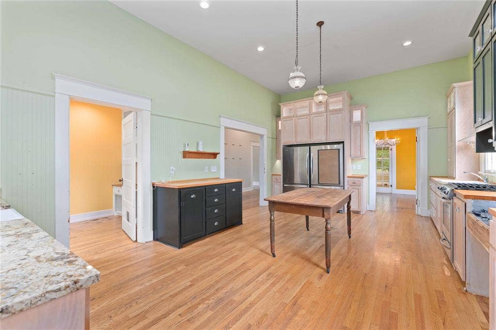 High-ceiling kitchen featuring wood-finish flooring, custom cabinetry with integrated stainless steel refrigerator, stone countertops, and decorative pendant lighting