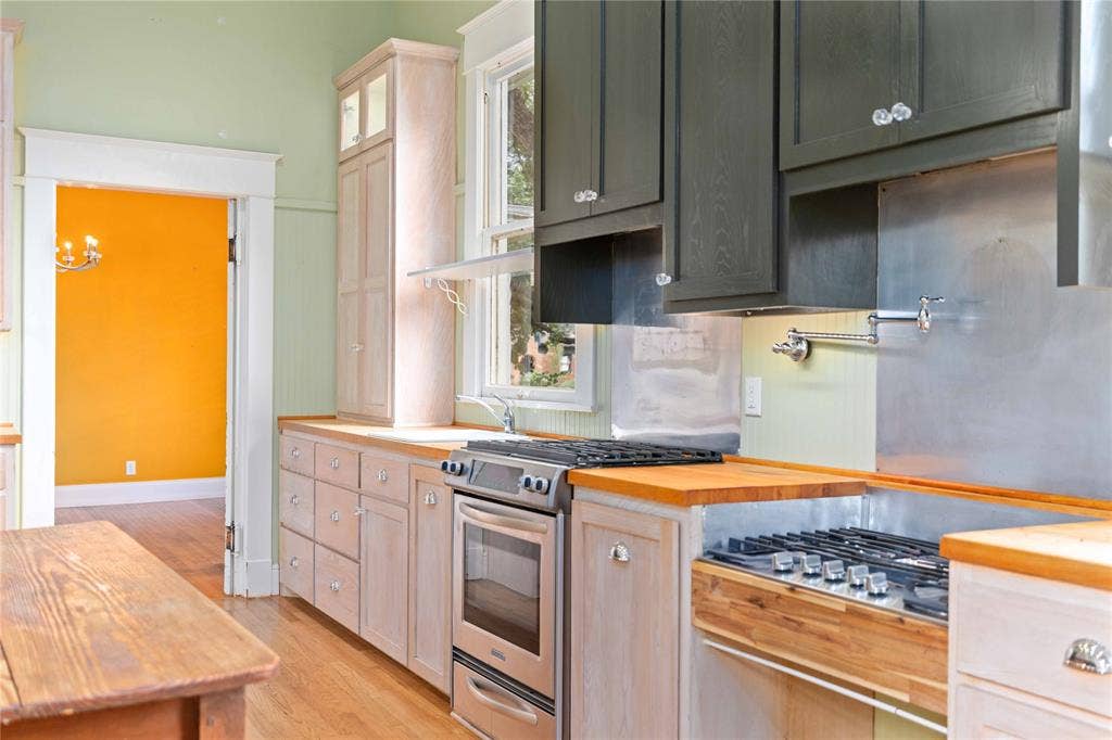 Kitchen featuring two-tone cabinetry, wood-finish countertops, stainless steel gas range, wall-mounted pot filler, and metal backsplash paneling