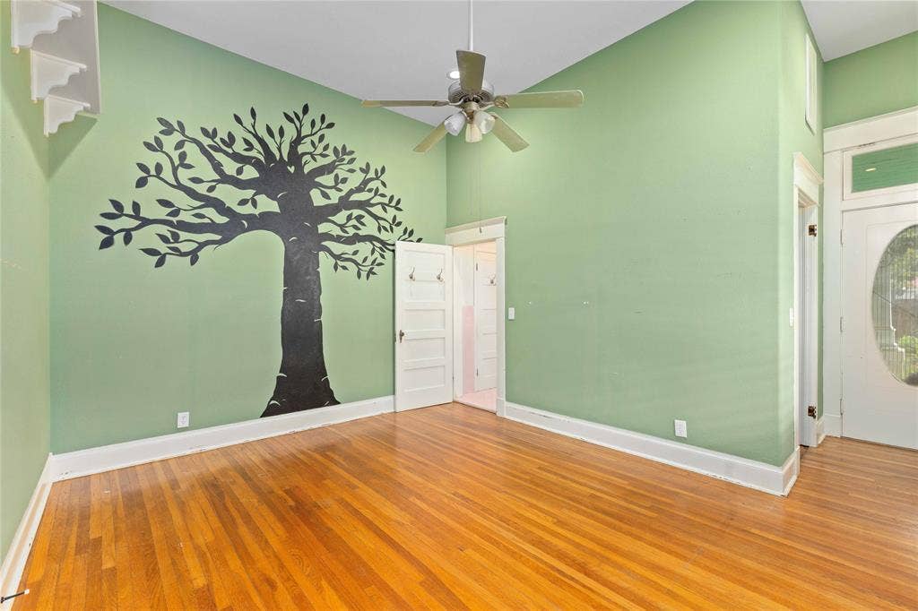 High-ceilinged room featuring wood-finish flooring, a multi-blade ceiling fan with integrated lighting, and a solid-core door with a transom window