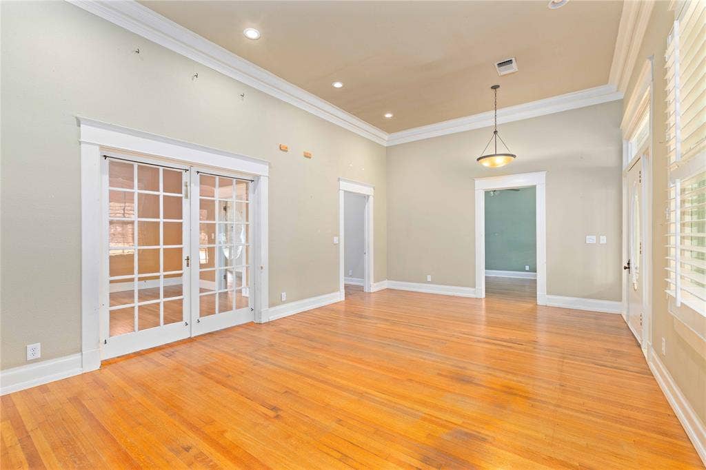 High ceilings with crown molding, wood-finish flooring, recessed lighting, double French doors, and a suspended pendant light fixture