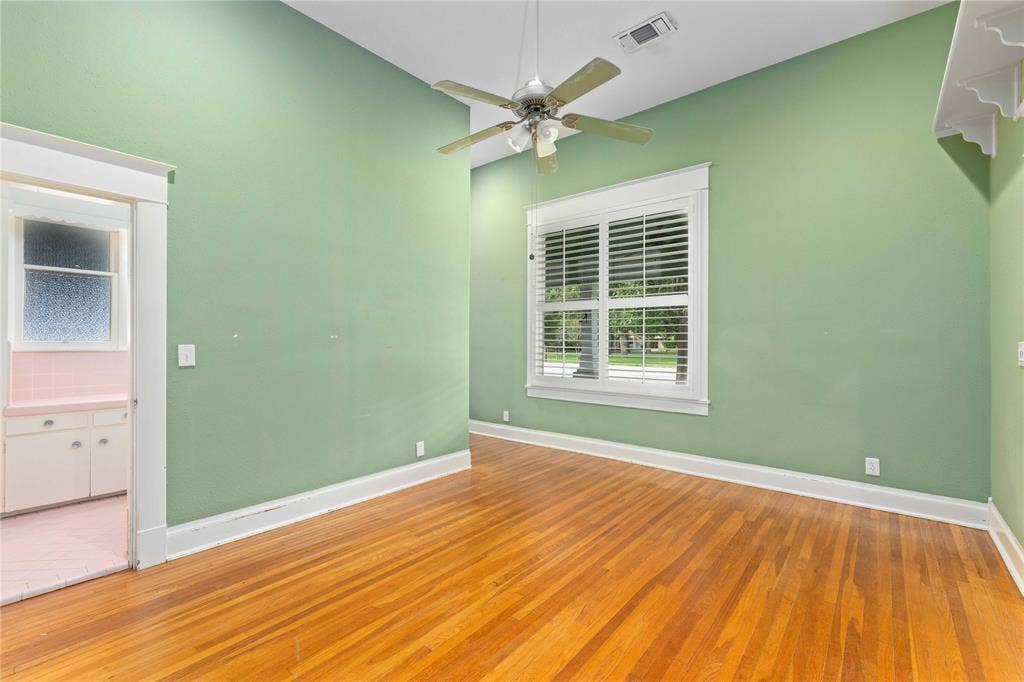 High-ceiling room featuring wood-finish flooring, multi-pane window with white shutters, and a ceiling-mounted fan with integrated light fixture