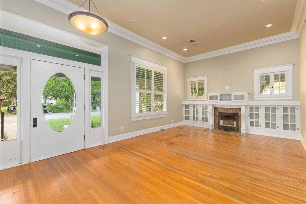 Wood-finish flooring, fireplace with white mantle and built-in glass-front cabinetry, crown molding, and recessed lighting