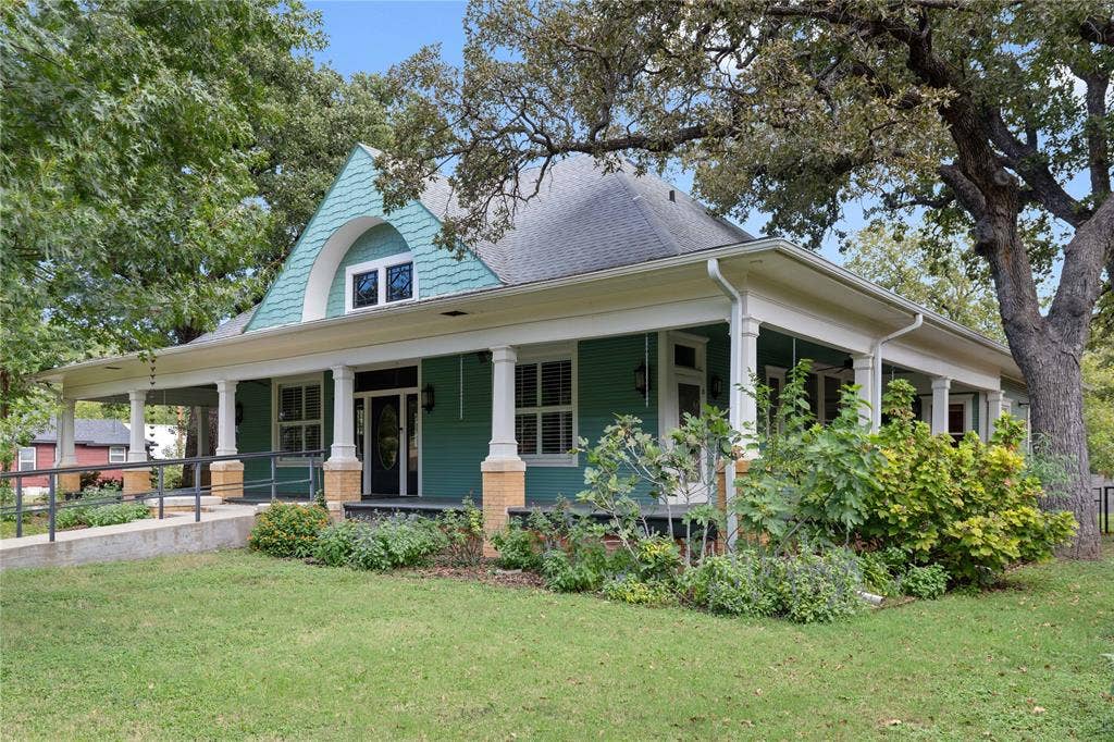 Craftsman-style residence featuring a wraparound porch, prominent arched gable detailing, shake-shingle siding, brick-base columns, and an exterior accessibility ramp
