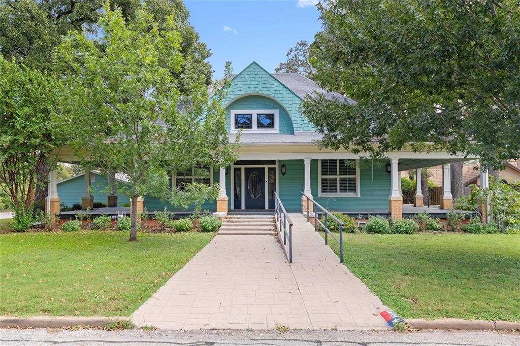 Craftsman-style exterior featuring shake siding, a wide wrap-around porch with classical columns, stone masonry accents, and a distinctive dormer window