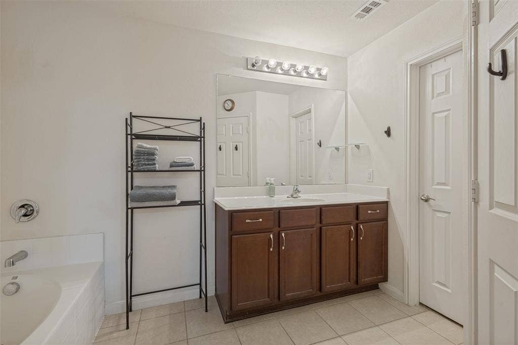 Bathroom featuring a dark wood vanity with a solid surface countertop, an expansive wall-mounted mirror, a five-bulb vanity light fixture, and tile flooring