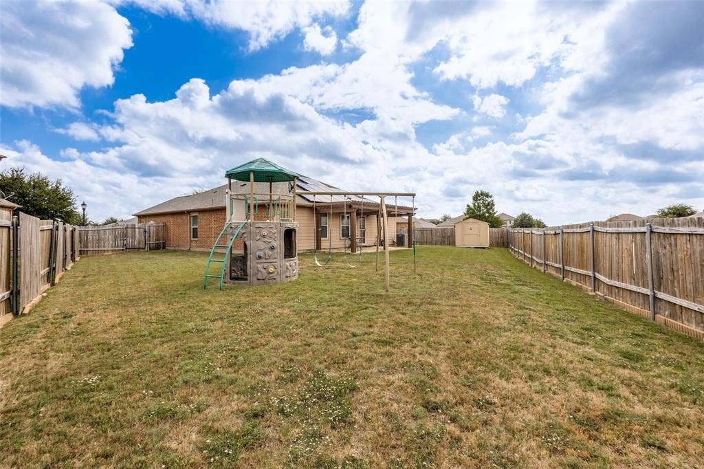 Expansive backyard featuring a sod lawn, wooden privacy fencing, a rear-facing covered patio, and a detached storage structure