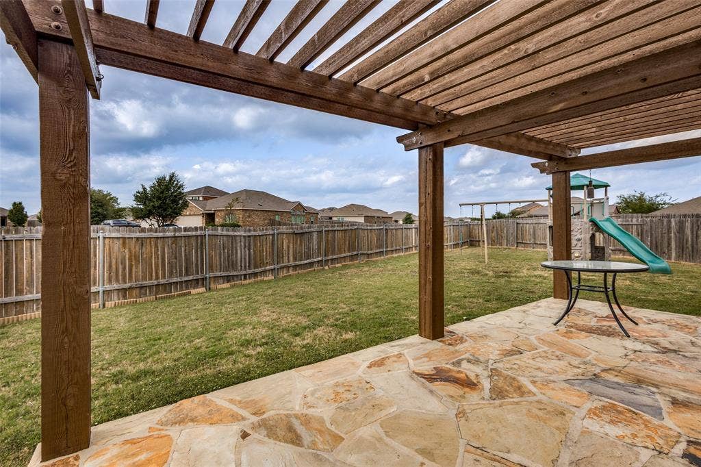 Outdoor living area featuring a wooden pergola, natural flagstone patio, and a fully fenced backyard