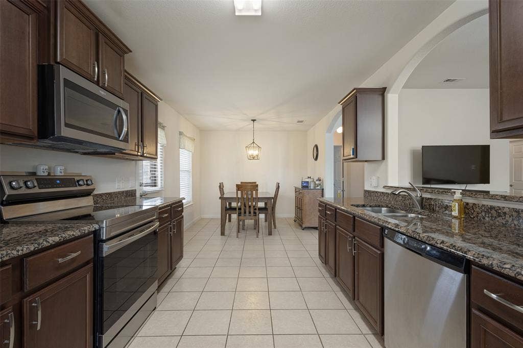 Kitchen featuring dark wood cabinetry, stone-surface countertops, stainless steel appliances, ceramic tile flooring, and an arched wall opening